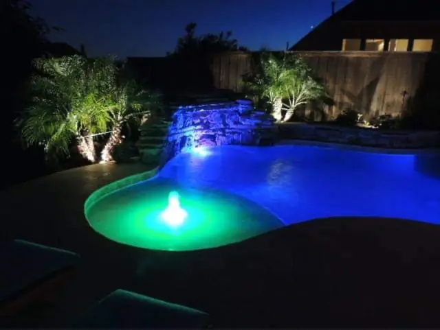 A North Texas pool at night with a lit stacked stone waterfall and blue and green LED lighting