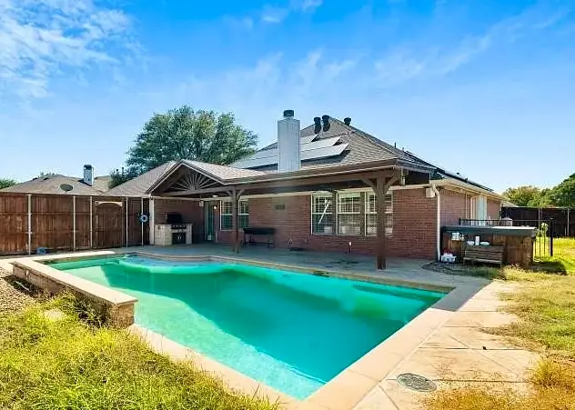 A brick house with a covered patio and a rectangular pool in a North Texas neighborhood