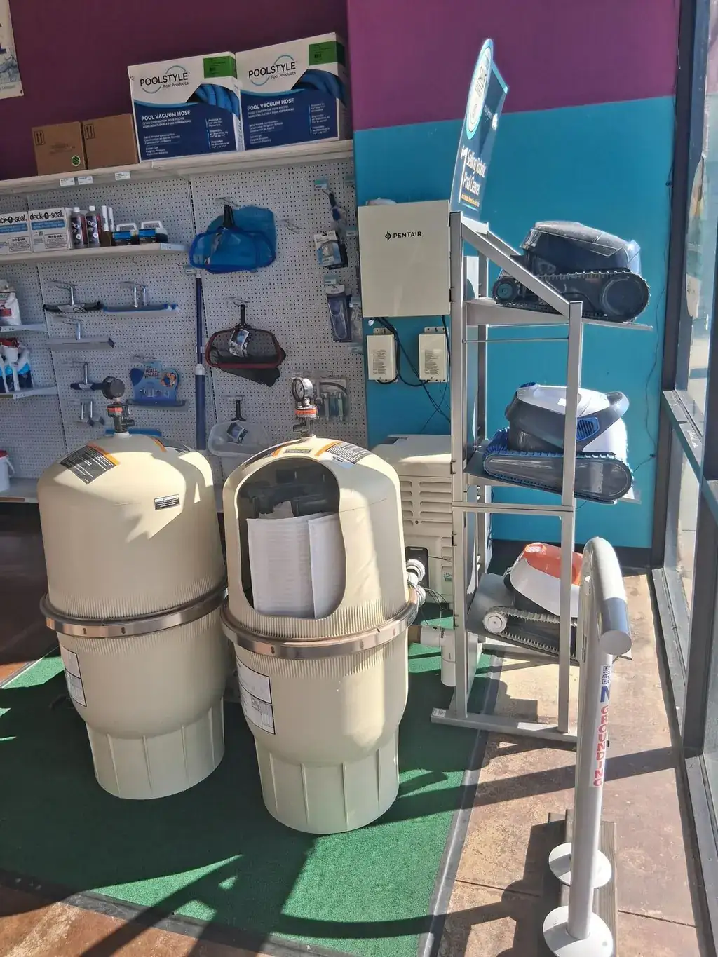 Filters and robotic pool cleaners on display next to a Pentair automation panel inside the store