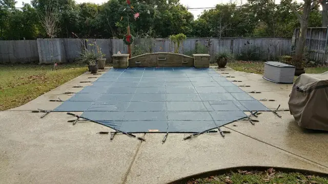 A pool under a navy mesh safety cover in late autumn